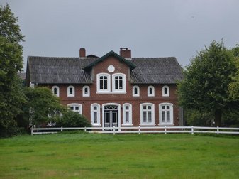 rotbraunes Steinhaus mit weißen Fensterrahmen - davor eine grüne Wiese